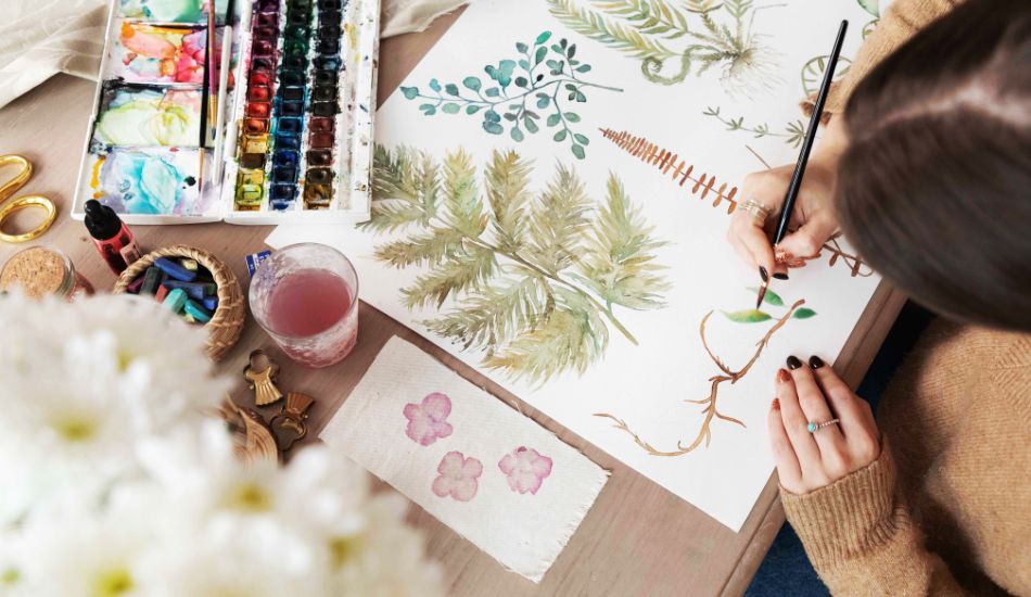 Woman using watercolour paints to create leaves and branches for products designed by a home décor wholesaler